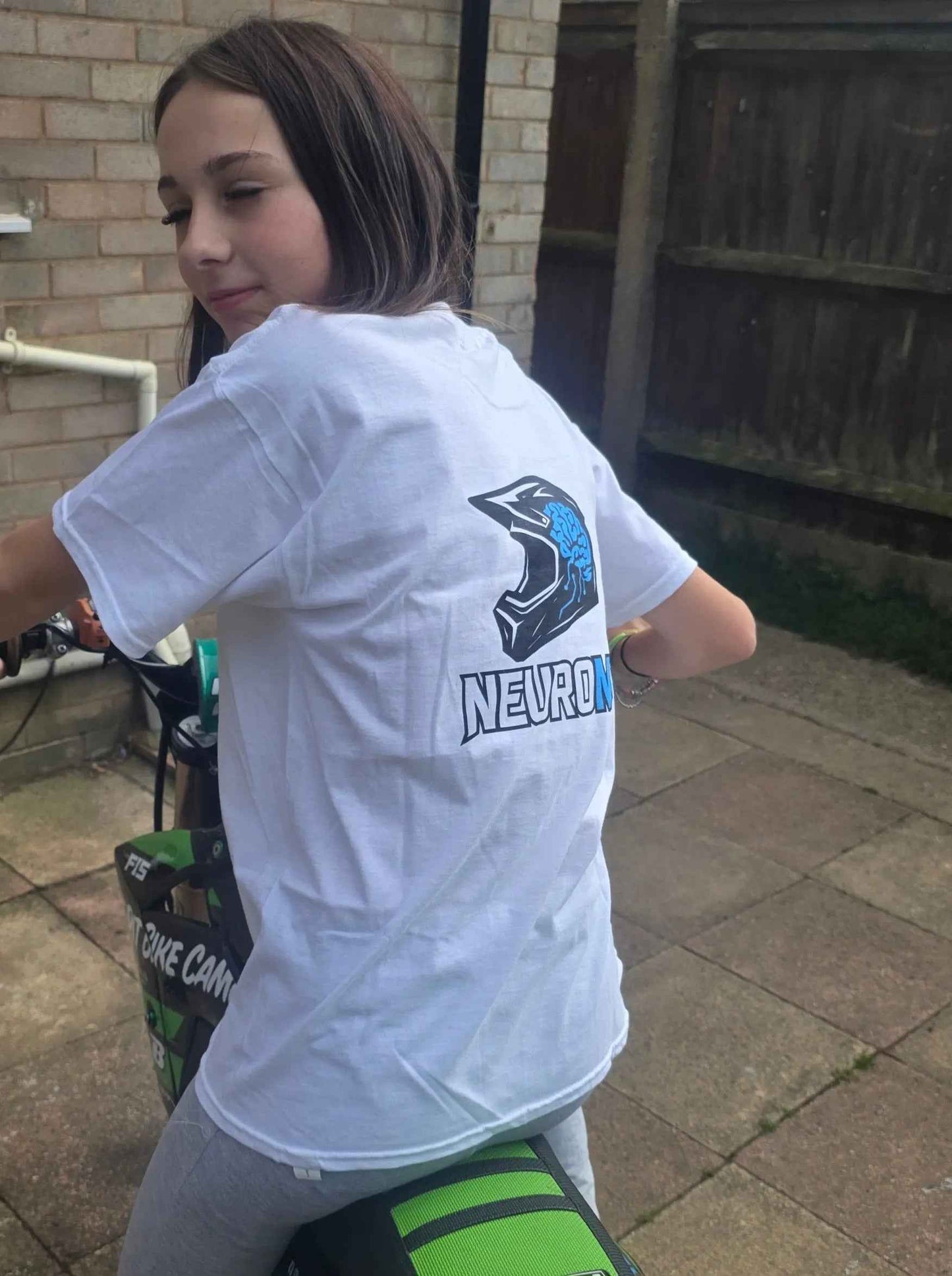 Girl in white motocross t-shirt with helmet and brain graphic, sitting on green dirt bike