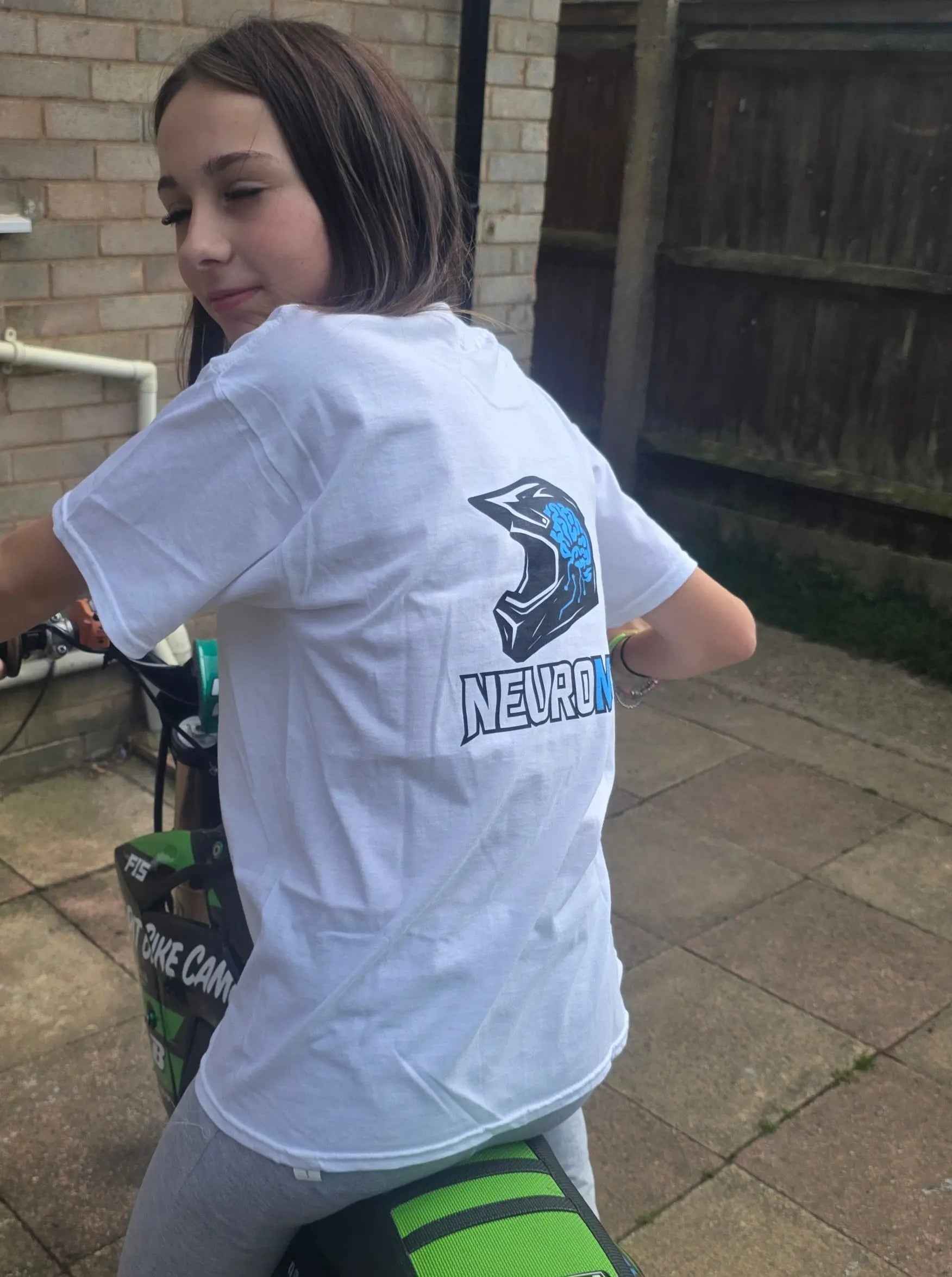 Girl in white motocross t-shirt with helmet and brain graphic, sitting on green dirt bike