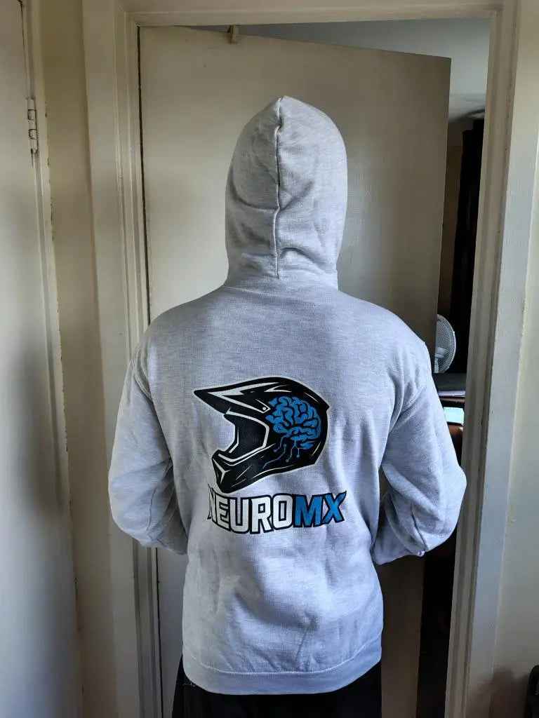 Person in gray hoodie with motocross helmet and blue brain graphic on back, NEUROMX logo.
