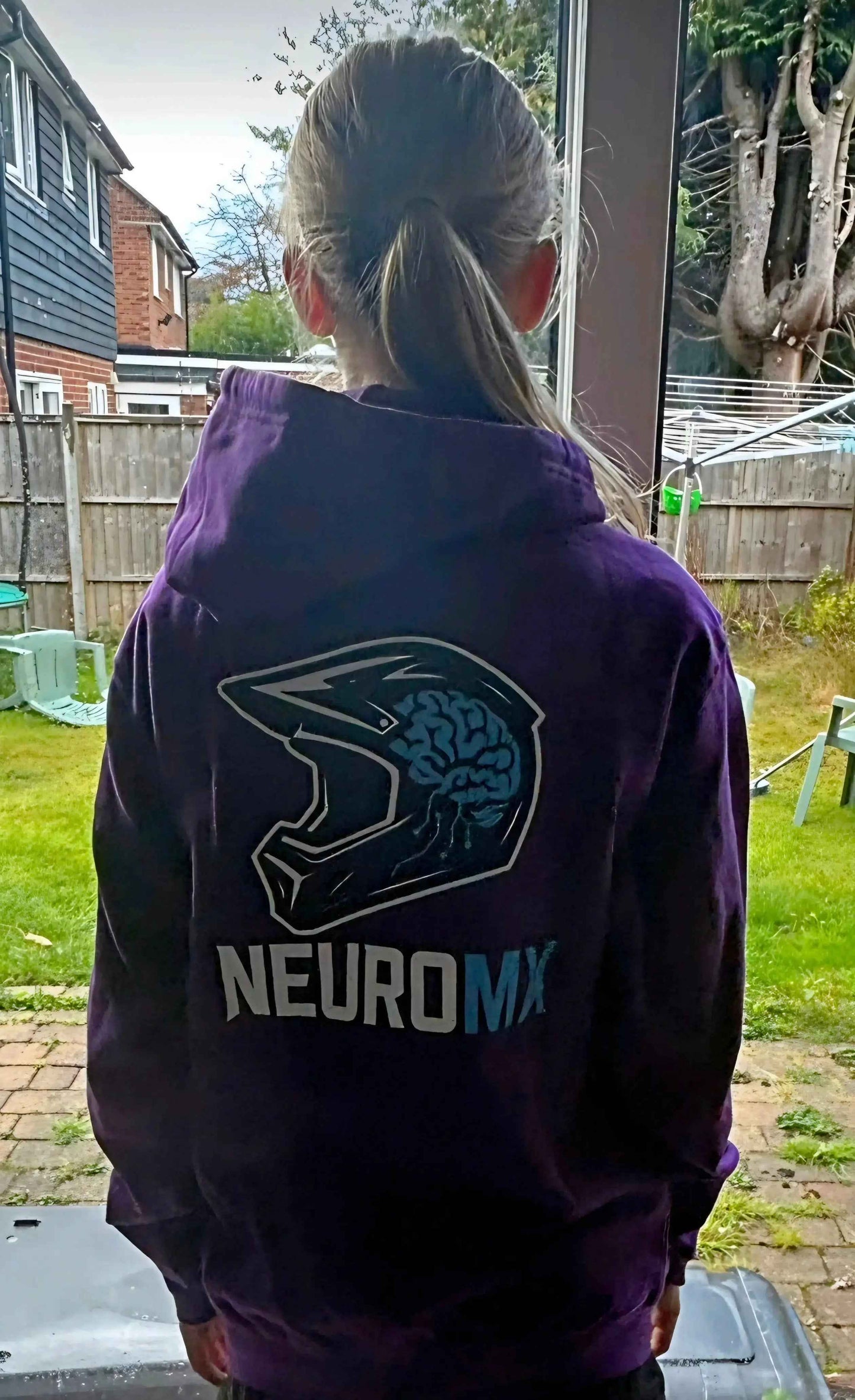 Person wearing purple motocross hoodie with helmet and brain graphic and NEUROMX text outdoors