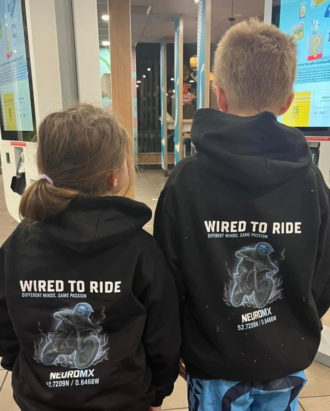 Two kids in black motocross hoodies with 'Wired to Ride' and a motocross rider graphic on the back.