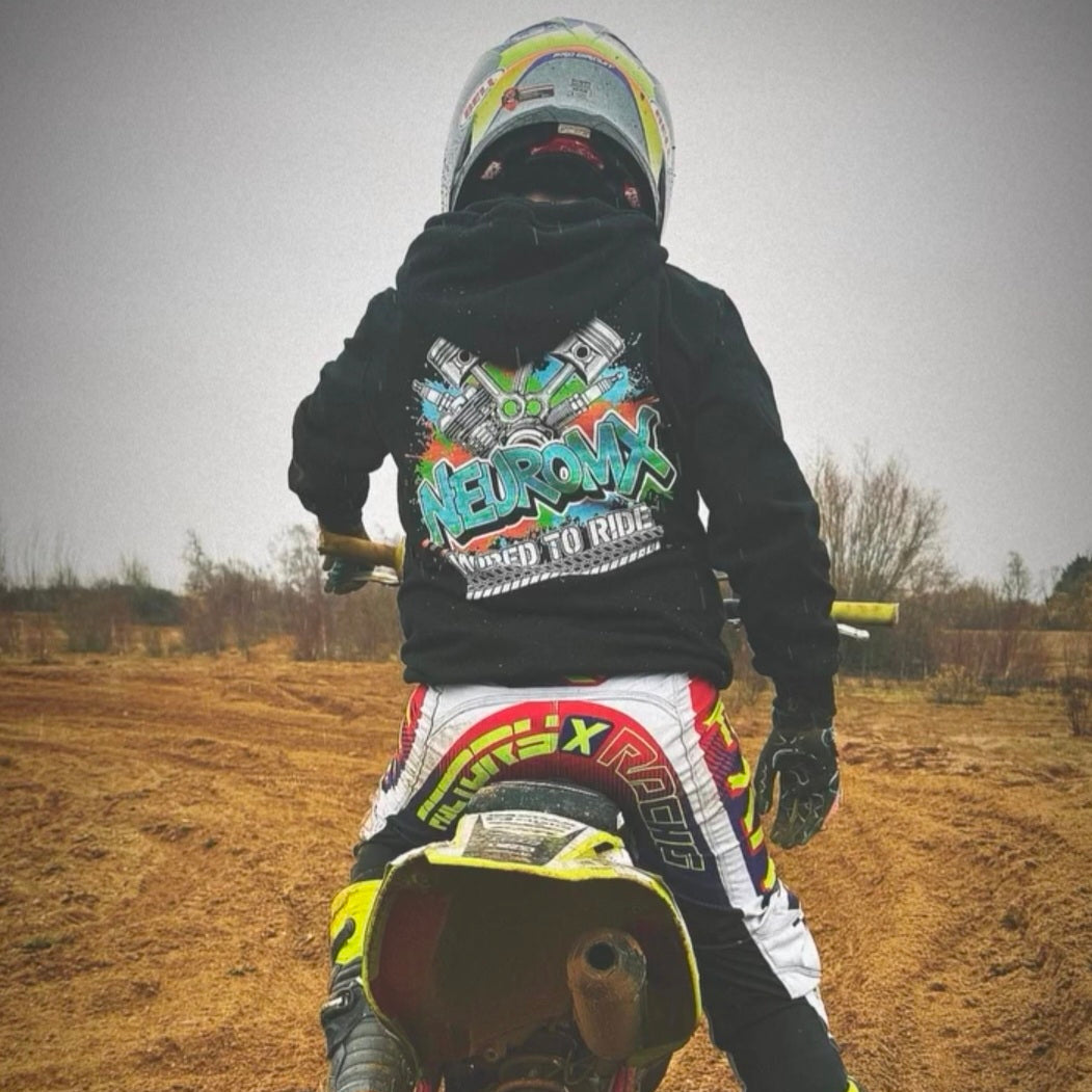 Motocross rider wearing graphic motocross hoodie and gear on dirt track, outdoor setting