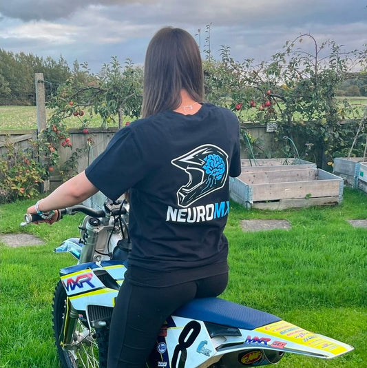 Woman in black NeuroMX motocross t-shirt sitting on dirt bike in garden setting