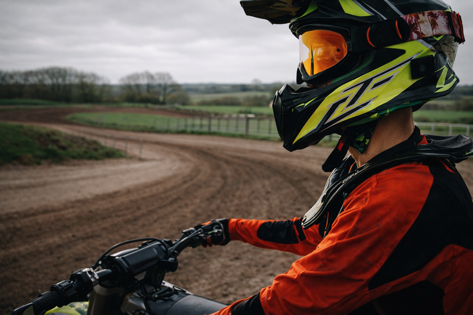 Person wearing a helmet and orange jacket on a motorcycle track