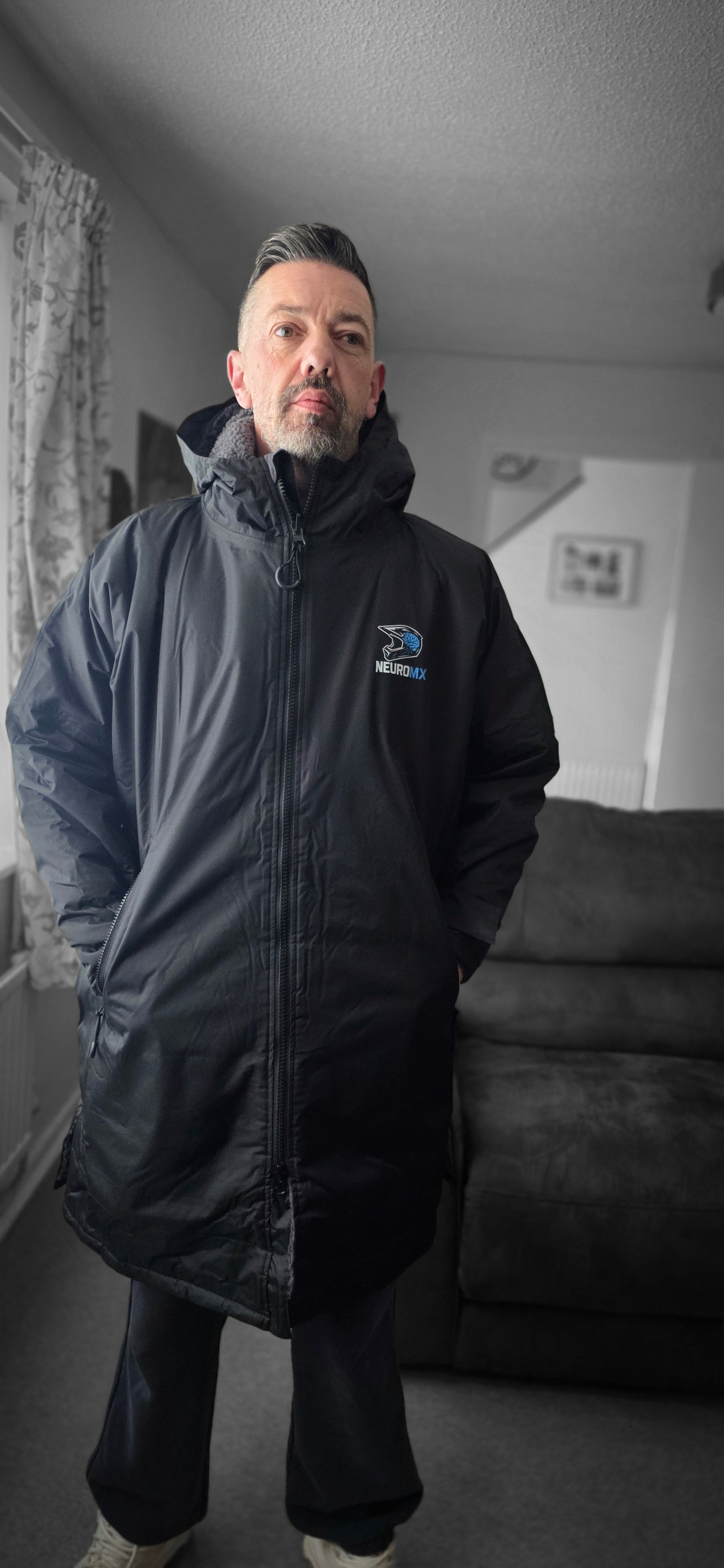 Man wearing black NeuroMX motocross parka jacket indoors, logo visible on chest