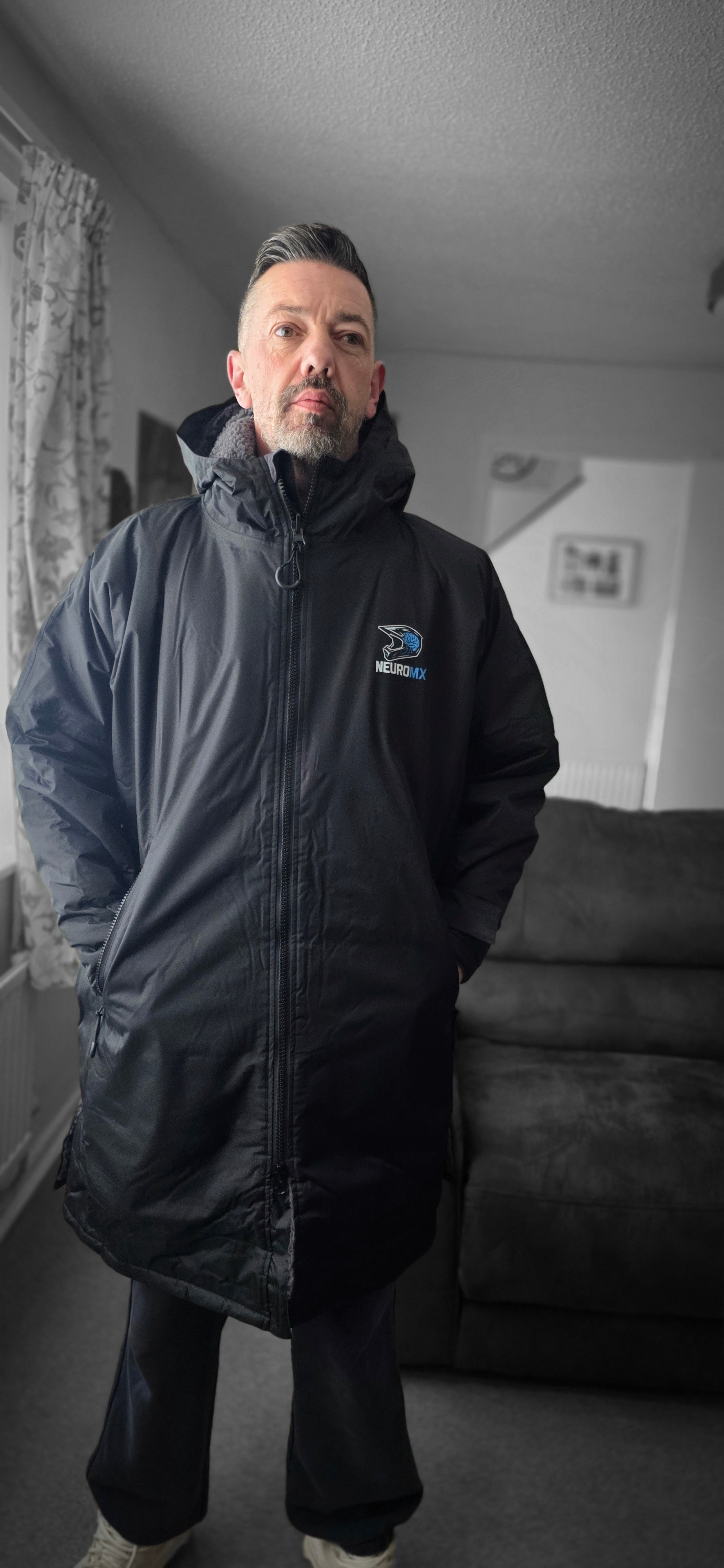 Man wearing black NeuroMX motocross parka jacket indoors, logo visible on chest